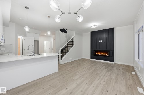Unfurnished living room with stairs, a large fireplace, and light wood-style floors - 53 Patriot Way, Spruce Grove, AB - Indoor Photo Showing Kitchen With Upgraded Kitchen