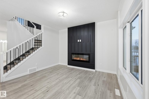 Unfurnished living room featuring stairway, light wood-style floors, and a fireplace - 53 Patriot Way, Spruce Grove, AB - Indoor With Fireplace