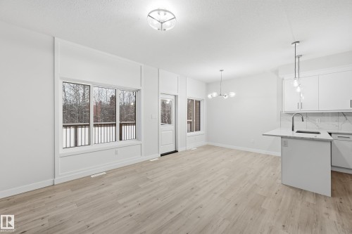 Kitchen with hanging light fixtures, white cabinetry, light wood-style flooring, light stone counters, and backsplash - 53 Patriot Way, Spruce Grove, AB - Indoor Photo Showing Kitchen