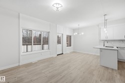Kitchen with hanging light fixtures, white cabinetry, light wood-style flooring, light stone counters, and backsplash - 