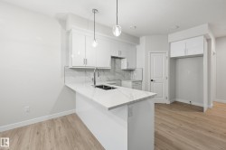 Kitchen with white cabinets, backsplash, a peninsula, light stone counters, and decorative light fixtures - 