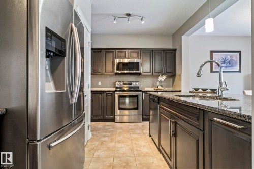 Kitchen with appliances with stainless steel finishes, pendant lighting, dark stone countertops, backsplash, and dark brown cabinetry - 5734 175A Avenue, Edmonton, AB - Indoor Photo Showing Kitchen With Upgraded Kitchen