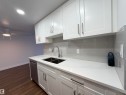 Kitchen with white cabinets, dishwasher, tasteful backsplash, light stone countertops, and dark wood-style floors - 103 10511 19 Avenue, Edmonton, AB 