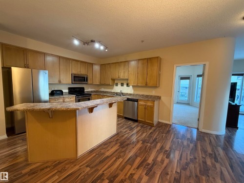 Kitchen with stainless steel appliances, a center island, dark wood-style flooring, a breakfast bar, and a textured ceiling - 321 4304 139 Avenue, Edmonton, AB - Indoor Photo Showing Kitchen