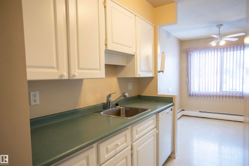 Kitchen with light floors, white dishwasher, ceiling fan, white cabinetry, and a baseboard heating unit - 207 11465 41 Avenue, Edmonton, AB - Indoor Photo Showing Kitchen