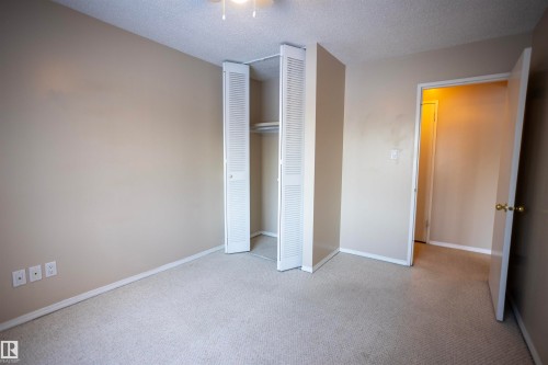 Unfurnished bedroom featuring a textured ceiling, light carpet, and a closet - 207 11465 41 Avenue, Edmonton, AB - Indoor Photo Showing Other Room