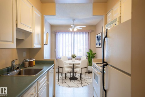 Kitchen featuring white appliances, white cabinetry, ceiling fan, a textured ceiling, and light floors - 207 11465 41 Avenue, Edmonton, AB - Indoor Photo Showing Kitchen