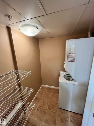 Laundry room featuring baseboards and stacked washer and dryer with extra storage - 405 10319 111 Street, Edmonton, AB - Indoor Photo Showing Laundry Room