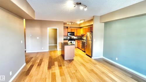 Kitchen with stainless steel appliances, brown cabinetry, a center island, a textured ceiling, and light wood finished floors - 405 10319 111 Street, Edmonton, AB - Indoor Photo Showing Other Room