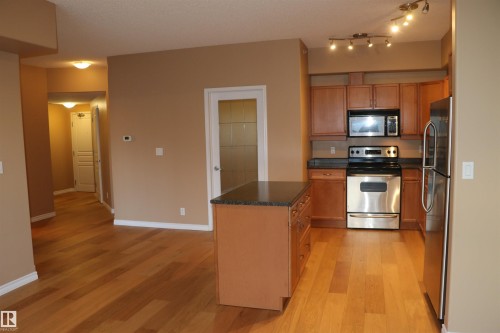 Kitchen featuring appliances with stainless steel finishes, light wood-style floors, brown cabinets, dark stone counters, and a textured ceiling - 405 10319 111 Street, Edmonton, AB - Indoor Photo Showing Kitchen