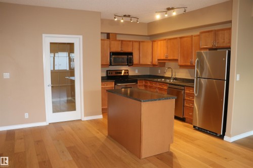 Kitchen with stainless steel appliances, light wood finished floors, a center island, brown cabinets, and dark stone counters - 405 10319 111 Street, Edmonton, AB - Indoor Photo Showing Kitchen With Double Sink