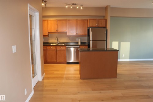 Kitchen featuring appliances with stainless steel finishes, dark stone countertops, light wood-type flooring, and brown cabinetry - 405 10319 111 Street, Edmonton, AB - Indoor Photo Showing Kitchen With Double Sink