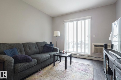 Living area with wood finished floors, baseboard heating, and a wall mounted AC - 407 812 Welsh Drive, Edmonton, AB - Indoor Photo Showing Living Room