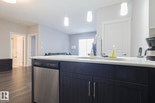 Kitchen featuring stainless steel dishwasher, light stone countertops, open floor plan, and hanging light fixtures - 407 812 Welsh Drive, Edmonton, AB - Indoor