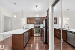 Kitchen featuring decorative light fixtures, a peninsula, appliances with stainless steel finishes, and dark wood-type flooring - 