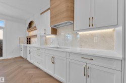 Kitchen featuring white cabinets, parquet floors, light stone countertops, backsplash, and range hood - 