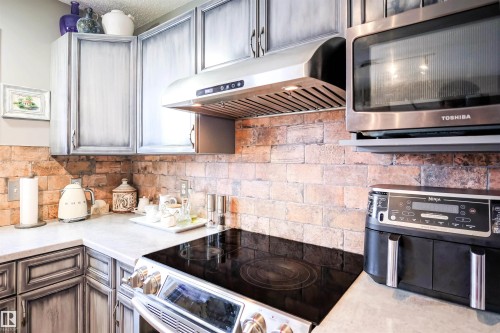 Kitchen featuring stainless steel microwave, electric stove, under cabinet range hood, gray cabinets, and backsplash - 5836 204 Street, Edmonton, AB - Indoor Photo Showing Kitchen