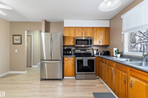 Kitchen with appliances with stainless steel finishes, brown cabinetry, light wood-style floors, and dark countertops - 17107 86 Avenue Nw, Edmonton, AB - Indoor Photo Showing Kitchen With Double Sink