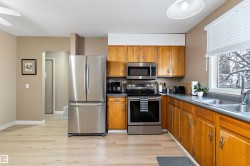 Kitchen with appliances with stainless steel finishes, brown cabinetry, light wood-style floors, and dark countertops - 