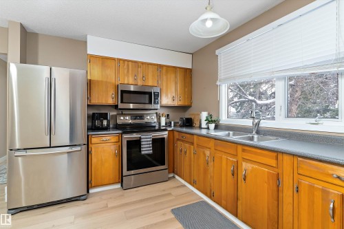 Kitchen with stainless steel appliances, brown cabinets, light wood-type flooring, dark countertops, and hanging light fixtures - 17107 86 Avenue Nw, Edmonton, AB - Indoor Photo Showing Kitchen With Double Sink