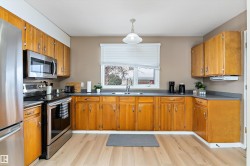 Kitchen with stainless steel appliances, dark countertops, hanging light fixtures, brown cabinets, and light wood finished floors - 