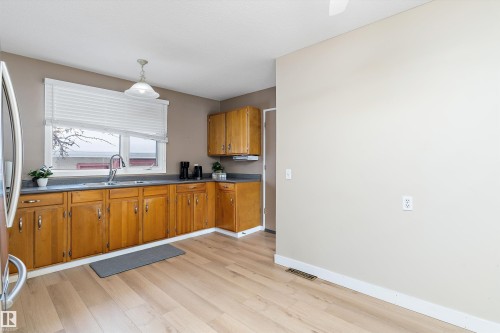 Kitchen with dark countertops, brown cabinets, pendant lighting, stainless steel refrigerator, and light wood-type flooring - 17107 86 Avenue Nw, Edmonton, AB - Indoor Photo Showing Kitchen With Double Sink
