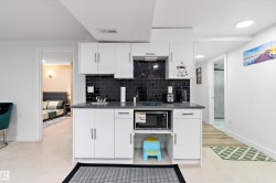 Kitchen with white cabinets, stainless steel microwave, decorative backsplash, recessed lighting, and dark stone countertops - 