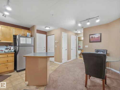 Kitchen featuring freestanding refrigerator, rail lighting, light countertops, light carpet, and a center island - 210 245 Edwards Drive, Edmonton, AB - Indoor Photo Showing Kitchen