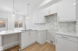 Kitchen with white cabinets, light stone counters, tasteful backsplash, light wood finished floors, and pendant lighting - 
