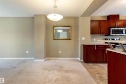 Kitchen featuring light countertops, appliances with stainless steel finishes, decorative light fixtures, dark brown cabinets, and light carpet - 