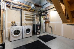 Laundry area featuring unfinished concrete flooring, heating unit, washing machine and clothes dryer, electric panel, and water heater - 
