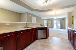 Kitchen with dark brown cabinets, dishwasher, decorative light fixtures, light colored carpet, and open floor plan - 