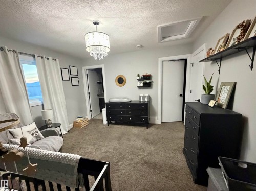 Carpeted bedroom featuring a textured ceiling, attic access, and a chandelier - 25 Harrison Gate, Spruce Grove, AB - Indoor