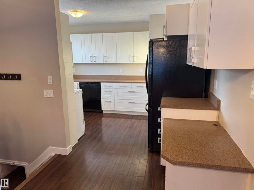 Kitchen with a textured ceiling, black appliances, white cabinets, and dark wood-style flooring - 21 Lundy Park Road, Stony Plain, AB - Indoor