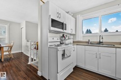 Kitchen with white appliances, white cabinetry, a textured ceiling, dark wood-type flooring, and light stone counters - 