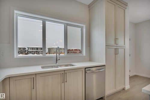 Kitchen featuring light brown cabinets, stainless steel dishwasher, light stone counters, and light wood-style flooring - 5742 Hawthorn Common, Edmonton, AB - Indoor Photo Showing Kitchen With Double Sink
