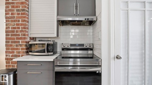 Kitchen featuring gray cabinets, stainless steel appliances, backsplash, and extractor fan - 9831 83 Avenue, Edmonton, AB - Indoor Photo Showing Kitchen