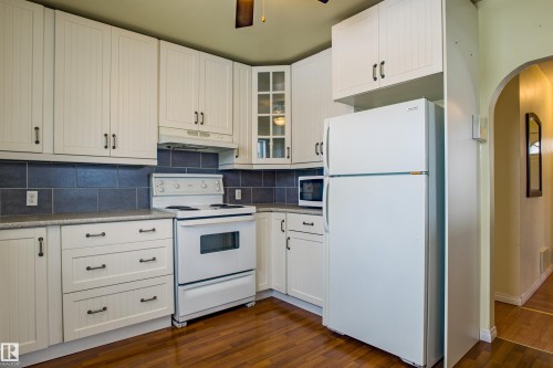 Kitchen featuring white appliances, arched walkways, white cabinets, and dark wood finished floors - 9228 124A Avenue, Edmonton, AB - Indoor Photo Showing Kitchen