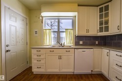 Kitchen featuring white dishwasher, glass insert cabinets, white cabinetry, dark wood-style flooring, and backsplash - 