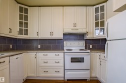 Kitchen with glass insert cabinets, white appliances, under cabinet range hood, and white cabinets - 