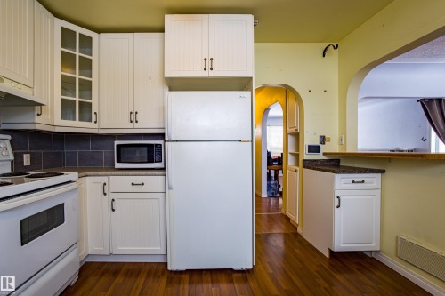 Kitchen with white appliances, glass insert cabinets, arched walkways, decorative backsplash, and white cabinets - 9228 124A Avenue, Edmonton, AB - Indoor Photo Showing Kitchen