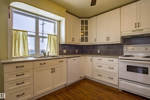 Kitchen with white appliances, under cabinet range hood, dark wood finished floors, tasteful backsplash, and glass insert cabinets - 9228 124A Avenue, Edmonton, AB - Indoor Photo Showing Kitchen With Double Sink