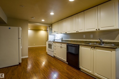 Kitchen with white appliances, recessed lighting, white cabinets, dark wood-style flooring, and dark countertops - 9228 124A Avenue, Edmonton, AB - Indoor Photo Showing Kitchen With Double Sink