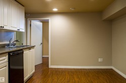 Kitchen featuring white cabinetry, dark countertops, black dishwasher, dark wood finished floors, and recessed lighting - 