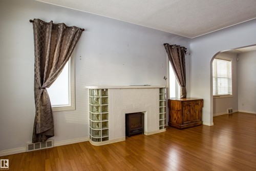 Unfurnished living room featuring arched walkways, a fireplace, wood finished floors, and a textured ceiling - 9228 124A Avenue, Edmonton, AB - Indoor