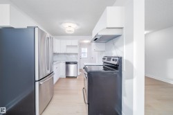 Kitchen featuring stainless steel appliances, light wood-type flooring, light countertops, white cabinets, and under cabinet range hood - 