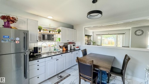 Kitchen featuring appliances with stainless steel finishes, light marble finish floors, white cabinets, dark stone countertops, and decorative backsplash - 12005 40 St, Edmonton, AB - Indoor