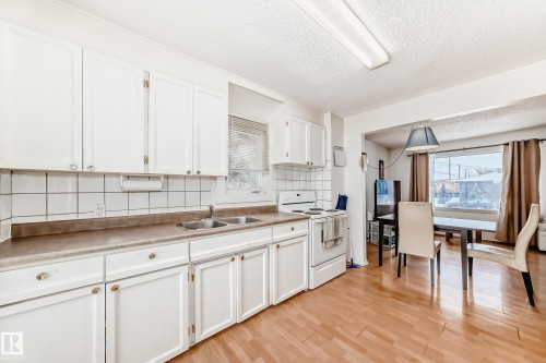 Kitchen with tasteful backsplash, white range with electric cooktop, a textured ceiling, white cabinetry, and healthy amount of natural light - 15515 92A Avenue, Edmonton, AB - Indoor Photo Showing Kitchen With Double Sink