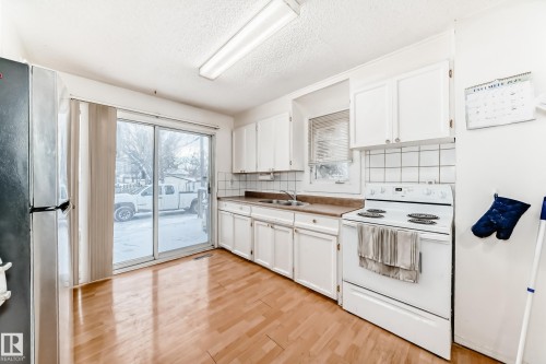 Kitchen with white range with electric stovetop, freestanding refrigerator, a textured ceiling, white cabinets, and light wood-style flooring - 15515 92A Avenue, Edmonton, AB - Indoor Photo Showing Kitchen With Double Sink