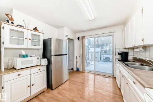 Kitchen with white cabinetry, glass insert cabinets, white microwave, freestanding refrigerator, and light countertops - 15515 92A Avenue, Edmonton, AB - Indoor Photo Showing Kitchen With Double Sink